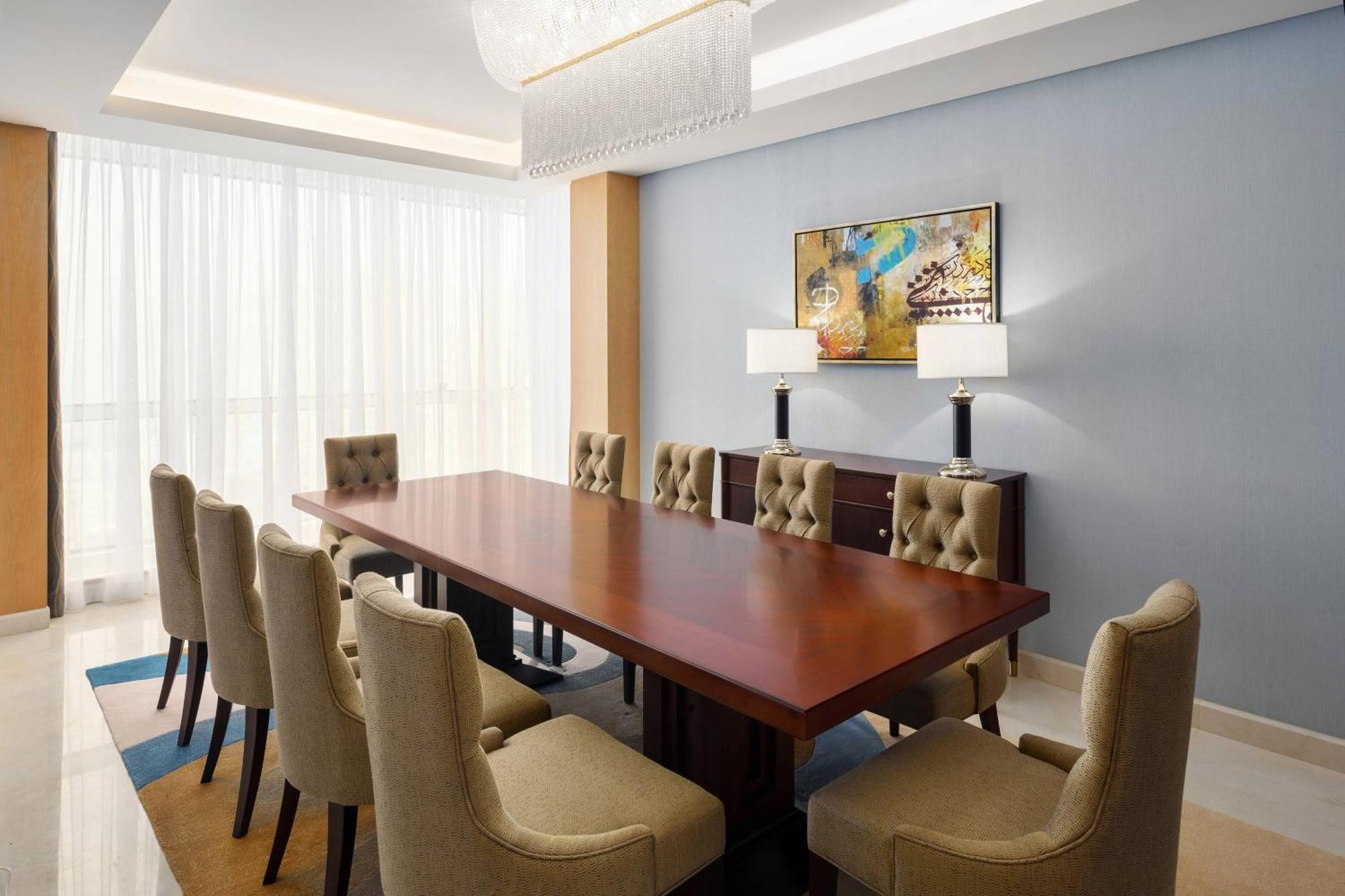 โรงแรมเชอราตัน มักกะฮ์ จาบาล อัล กาบา Mecca ภายนอก รูปภาพ The photo shows a spacious and elegantly designed conference room. It features a large wooden conference table surrounded by upholstered chairs. The chairs have a beige color and a tufted design. On one side of the room, there are two contemporary la