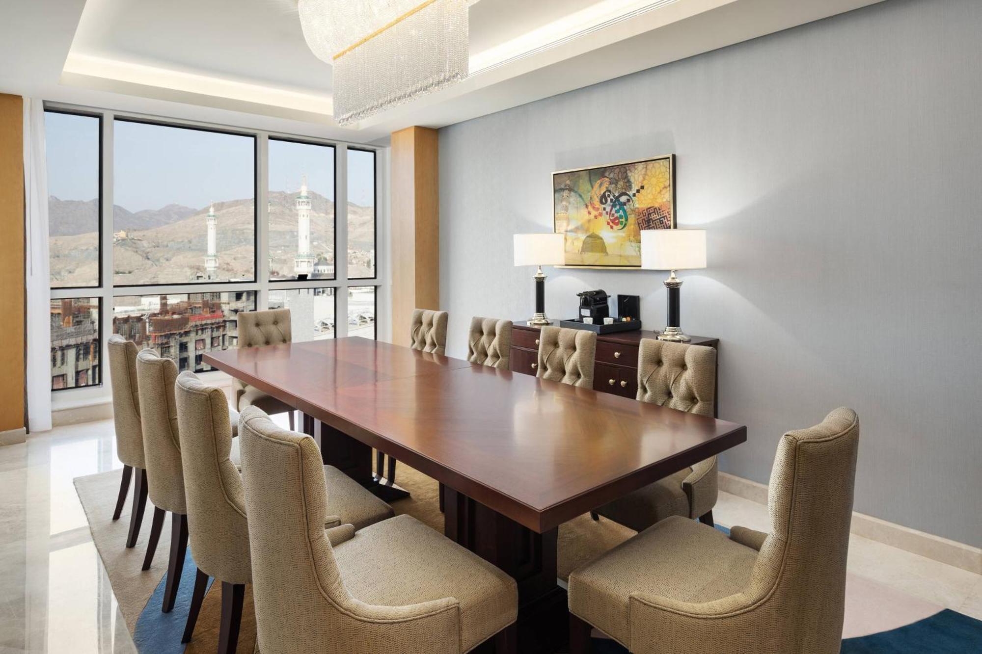 โรงแรมเชอราตัน มักกะฮ์ จาบาล อัล กาบา Mecca ภายนอก รูปภาพ The photo shows a modern conference room with a large wooden table surrounded by upholstered chairs. The room is well-lit, featuring large windows that offer a view of the outdoors, possibly with mountains in the background. On one wall, there is a p